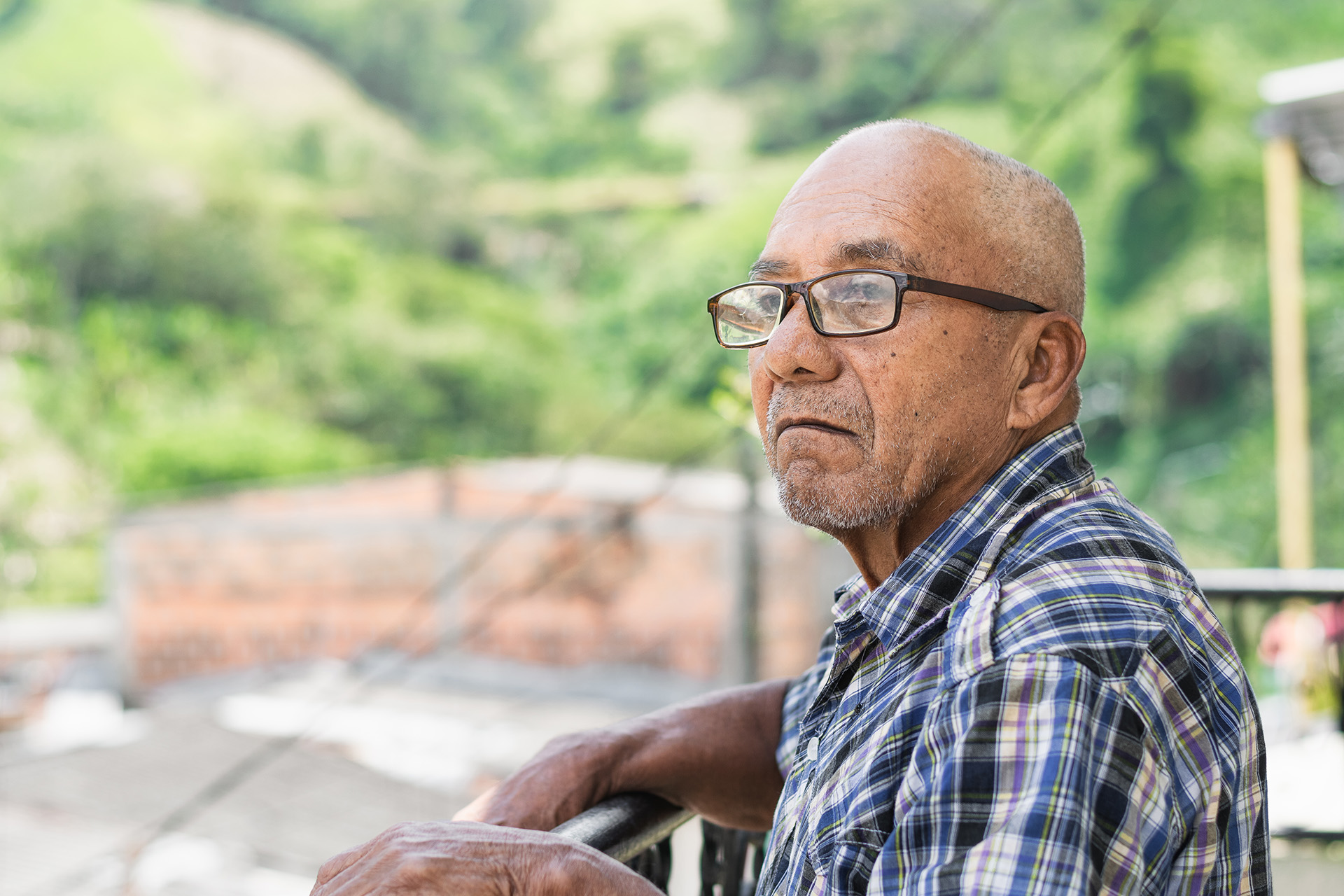 close-up of an elderly latin man with brown skin and glasses, st an elderly man looks out at the distance and contemplates life