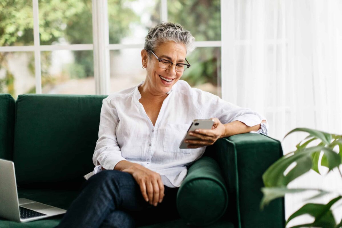 A female Medicare member uses the Pyx Health app while sitting on a sofa.