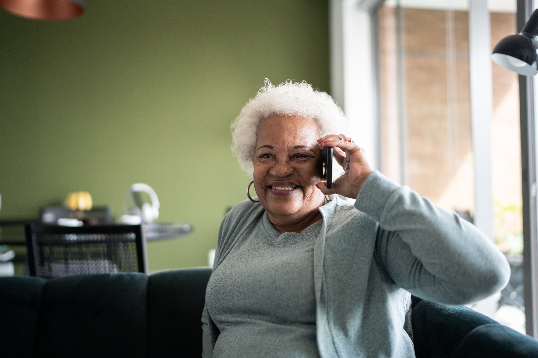Senior woman talking on the phone at home an older gentleman and a caregiver sit in nature staring out into the distance.