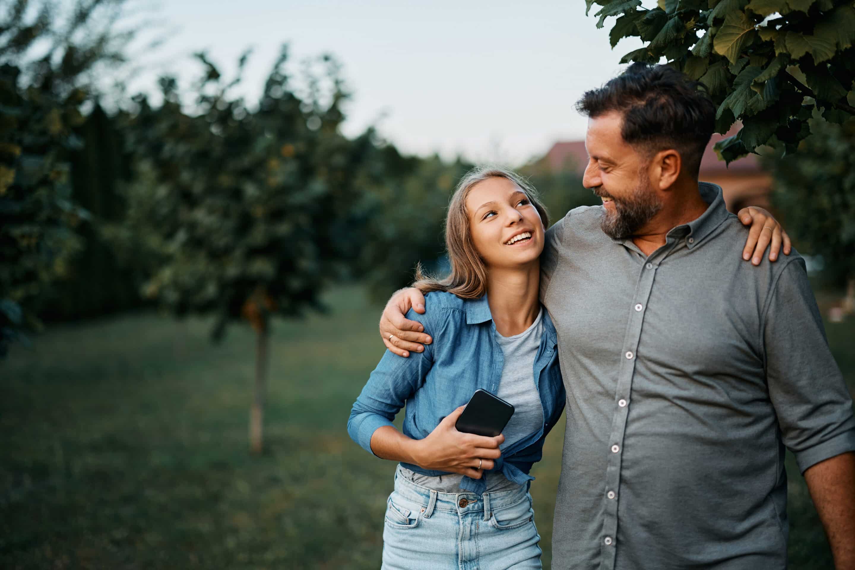 Happy man talking to his teenage daughter in the backyard. an older gentleman and a caregiver sit in nature staring out into the distance.