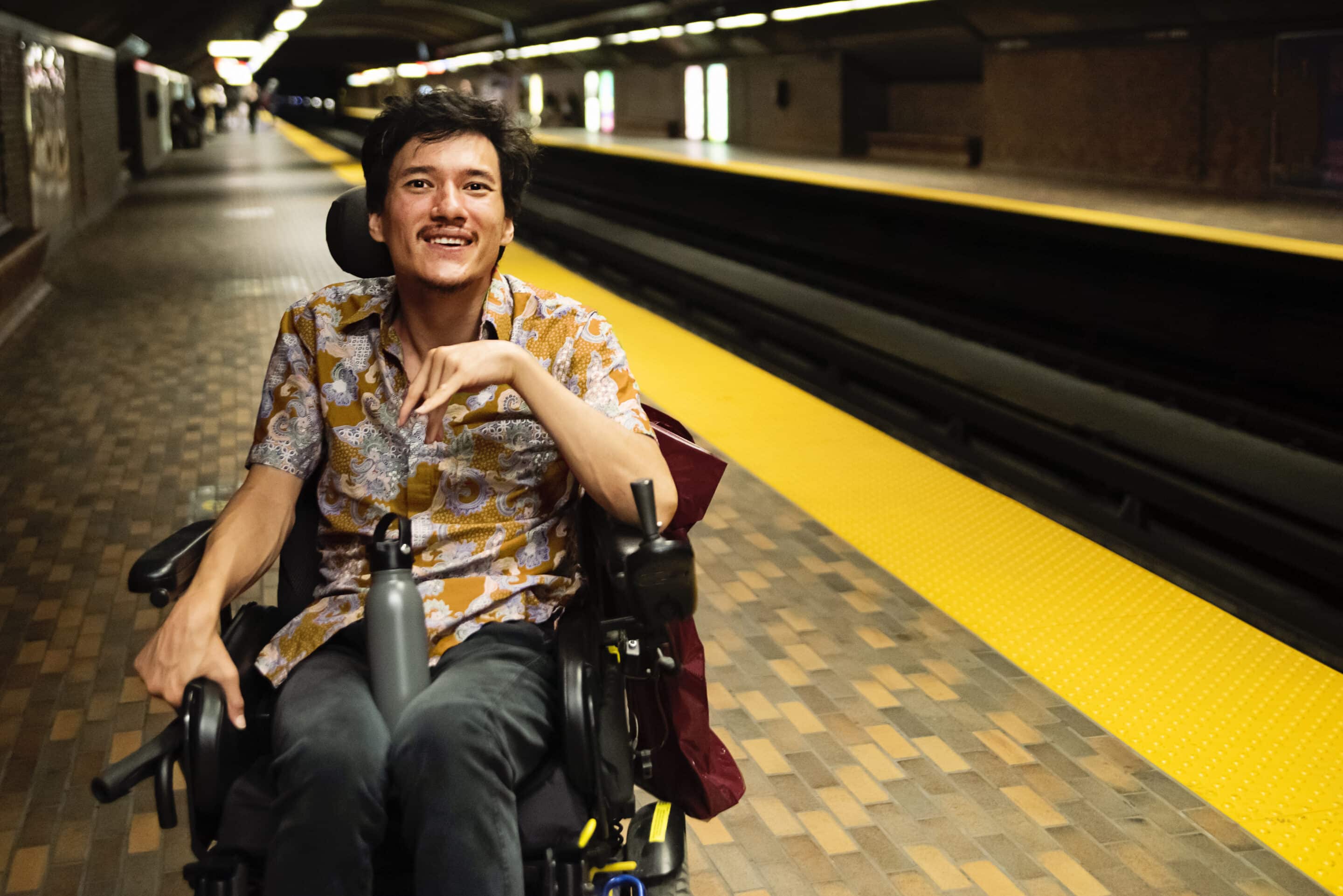 Young asian man using a wheelchair in a subway station. older woman staring out of a window