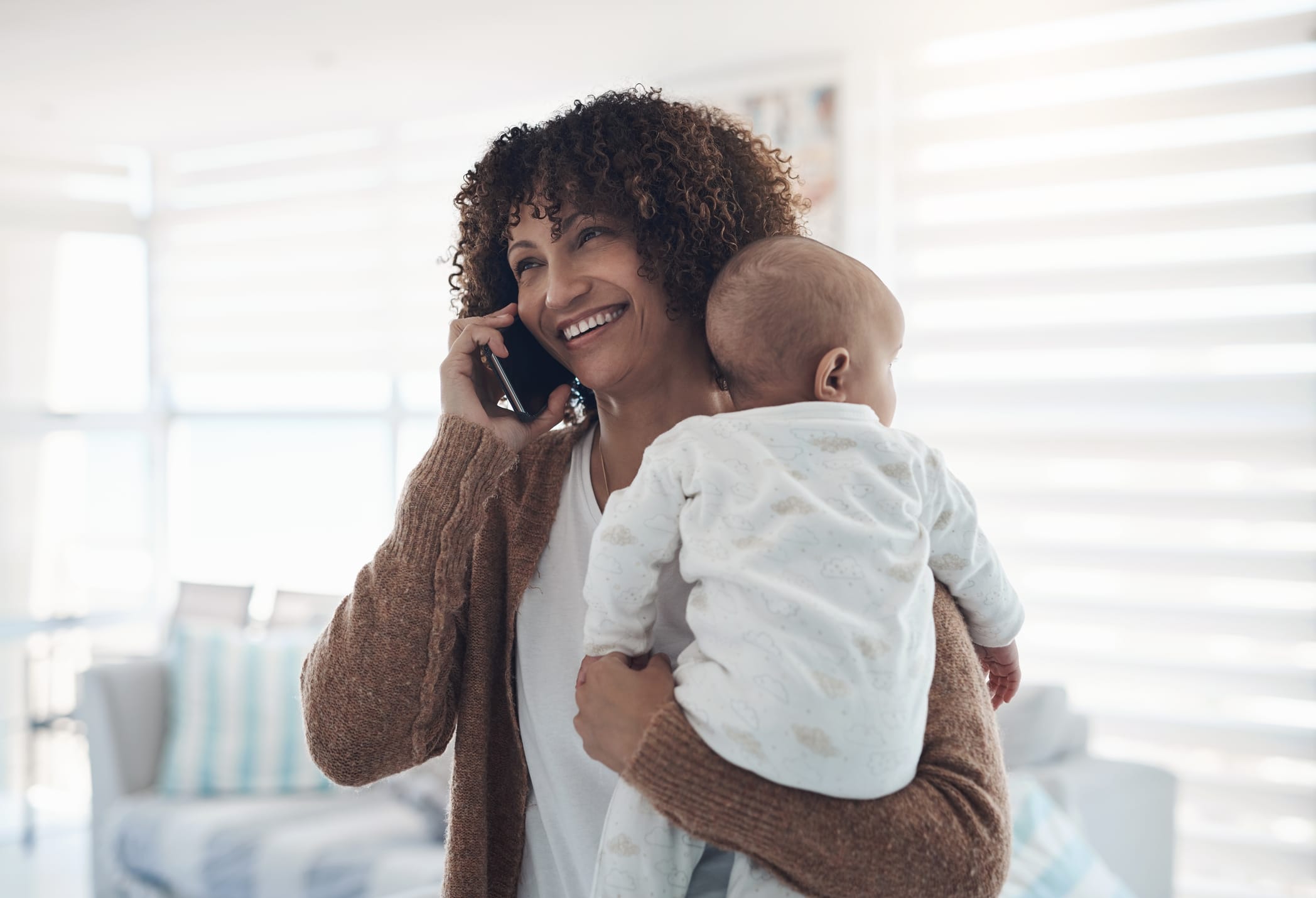Shot of a young woman using a smartphone while carrying her adorable baby girl at home mother holding baby and talking on a cell phone